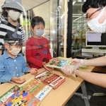 マスク姿で手袋をはめた図書館職員から予約していた本を受け取る子どもたち＝１７日午前、神戸市中央区楠町７、市立中央図書館（撮影・後藤亮平）