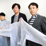 かばんの縫製技術を生かした医療用ガウンを手にする兵庫県鞄工業組合の由利昇三郎理事長（中央）ら＝豊岡市役所