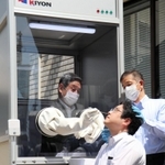 ウオークスルー方式で、ボックス内から検体を取る動作を見せる神戸市医師会の置塩隆会長（左奥）＝神戸市中央区