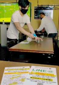 開店前に店内を清掃する店員。机にはコロナ対策を伝えるパネルを置く＝神戸市中央区中山手通１、スポーツバー「ディーフェンス」