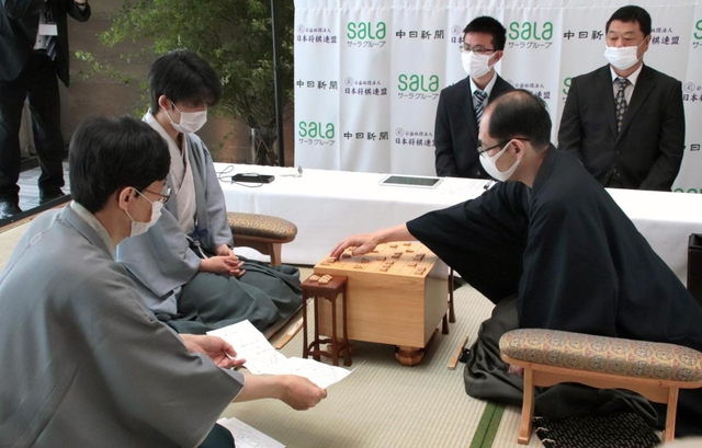 王位戦第１局で、立会人の谷川浩司九段（手前）から封じ手が示され対局を再開する木村一基王位（右）と藤井聡太七段＝２日午前、愛知県豊橋市、ホテルアークリッシュ豊橋