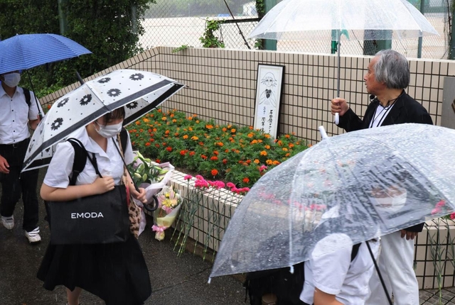 校門前に花を供え、追悼の言葉を述べる参加者＝６日午前、神戸市西区美賀多台９、神戸高塚高校（撮影・吉田敦史）