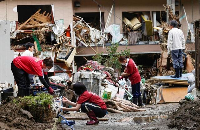 豪雨で氾濫した球磨川の水が押し寄せ、２階の窓から椅子や木材が飛び出した建物と、水に漬かった家財を片付ける家族ら＝１０日午前９時２５分、熊本県八代市