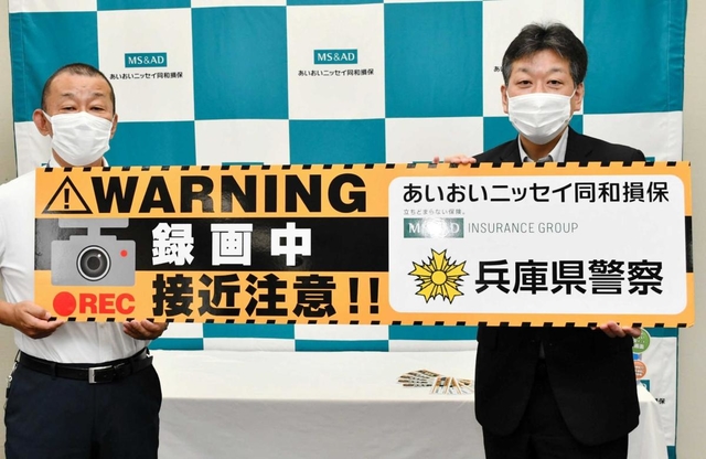 ステッカーを模したパネルを持つあいおいニッセイ同和損害保険の中村哲神戸支店長（右）と兵庫県警の矢野浩司交通部長＝神戸市中央区明石町