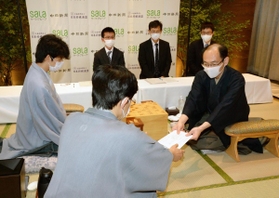 王位戦第１局で、立会人の谷川浩司九段（手前）に封じ手を渡す木村一基王位（右）。左は藤井聡太七段＝１日午後、愛知県豊橋市、ホテルアークリッシュ豊橋