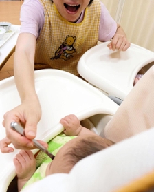 子どもに離乳食を食べさせる院内保育所の保育士。笑顔でそしゃくをする様子を見せると食べさせやすく、マスクは外す＝神戸市内