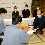王位戦第１局で、立会人の谷川浩司九段（手前）に封じ手を渡す木村一基王位（右）。左は藤井聡太七段＝１日午後、愛知県豊橋市、ホテルアークリッシュ豊橋