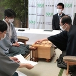 王位戦第１局で、立会人の谷川浩司九段（手前）から封じ手が示され対局を再開する木村一基王位（右）と藤井聡太七段＝２日午前、愛知県豊橋市、ホテルアークリッシュ豊橋