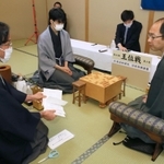 王位戦第２局で、立会人の深浦康市九段（左）から封じ手を示される木村一基王位（右）。左から２人目は藤井聡太七段＝１４日午前、札幌市、ホテルエミシア札幌