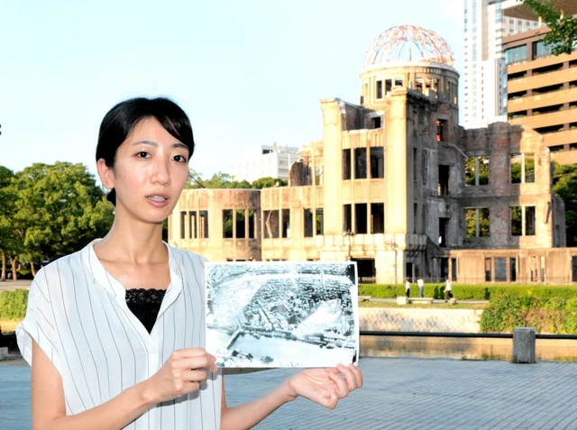 ピースボランティアの松本愛美さん。「平和記念公園は、昔は中島地区という住宅街だった」と写真を持って説明する＝広島市中区中島町、平和記念公園