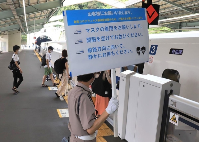 帰省客らに感染予防を呼びかける掲示板を持つ警備員＝８日午前、神戸市中央区、ＪＲ新神戸駅（撮影・斎藤雅志）