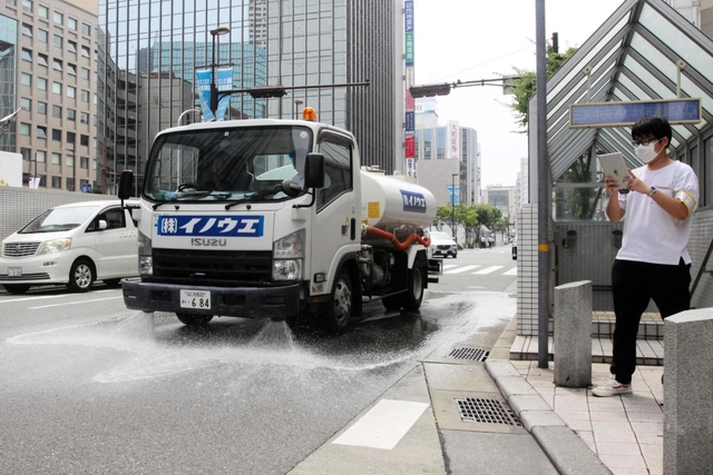路面を冷やすため、水をまきながら走る散水車。右は温度の変化を記録する神戸大の学生＝神戸市中央区三宮町１