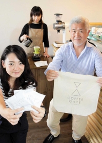 「ＣＯＦＦＥＥ　ＧＡＴＥ」のロゴマーク入りグッズを手にする左野徳夫社長（右）ら＝西宮市本町
