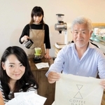 「ＣＯＦＦＥＥ　ＧＡＴＥ」のロゴマーク入りグッズを手にする左野徳夫社長（右）ら＝西宮市本町