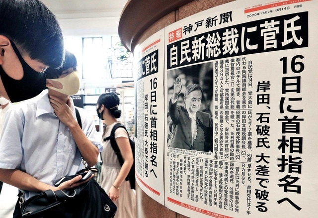 新総裁選出を伝える号外に足を止める人たち＝１４日午後、ＪＲ神戸駅（撮影・鈴木雅之）