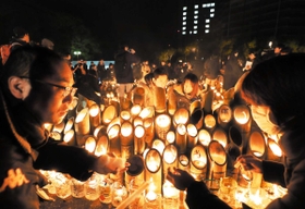 ろうそくを分け合い、竹灯ろうに明かりをともす人たち＝２０２０年１月１７日、神戸市中央区、東遊園地