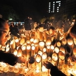 ろうそくを分け合い、竹灯ろうに明かりをともす人たち＝２０２０年１月１７日、神戸市中央区、東遊園地