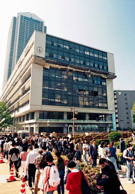 ６階部分が押しつぶされた神戸市役所２号館。ポートアイランドへ向かう代替バスを待つ列が続いた＝１９９５年５月１０日