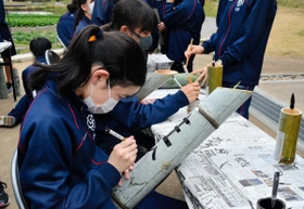竹灯籠に筆で丁寧に文字を書き込む生徒たち＝神戸市北区山田町藍那