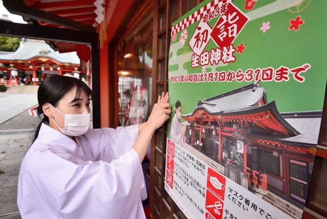初詣の「分散参拝」やマスク着用を呼び掛けるポスターを張る巫女（みこ）＝神戸市中央区下山手通１、生田神社（撮影・秋山亮太）