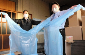 在庫の医療用ガウンを持つタニー・パックの宮口正人取締役（左）と、服部の入梅功・衛生商品担当マネジャー＝豊岡市元町