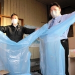 在庫の医療用ガウンを持つタニー・パックの宮口正人取締役（左）と、服部の入梅功・衛生商品担当マネジャー＝豊岡市元町