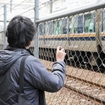 通過するＪＲの電車を見つめるＢさん。事故で背骨を骨折。後遺症で首から腰に痛みが残り、背中には湿布薬の跡が染み付いている＝伊丹市内