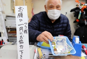 日々、大量の小銭を扱うという花崎治良さん。レジ前の立て札で協力を求める＝神戸市兵庫区東山町１