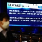緊急事態宣言の延長決定のニュースを伝える大型ビジョン前を歩くマスク姿の男性＝２日夜、神戸市中央区雲井通７（撮影・秋山亮太）