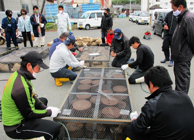 金属製の籠に肥料を入れる育波浦漁協青年部のメンバーら。手前は栄養塩を含む固形肥料、奥は農耕用が入った麻袋を搭載した＝２０２０年１１月、淡路市育波（同市提供）