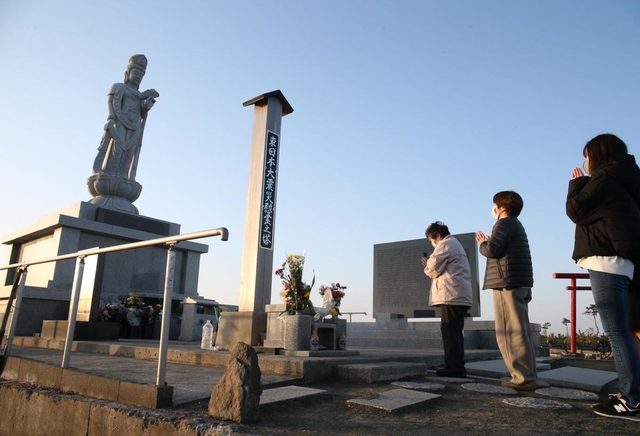 津波犠牲者を追悼する慰霊の塔を訪れ、手を合わせる人たち。すぐそばの波打ち際から潮騒がとどろく＝１１日午前６時２８分、仙台市若林区荒浜（撮影・小林良多）