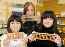 神山川の桜で作られたそろばんを手に持つ木村祐子さん（中央）とそろばん教室の児童ら＝宮城県気仙沼市本吉町窪