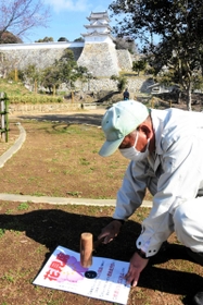 兵庫県立明石公園の地面に「花見席」の張り紙を打ち付ける作業員＝２４日、明石市内