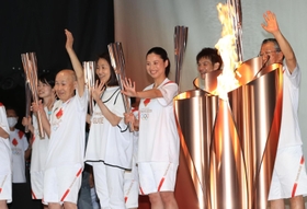 聖火を囲んで笑顔で手を振る聖火リレーのランナーたち。中央は北京五輪５千メートル代表の小林祐梨子さん＝２３日午後、姫路市本町（撮影・小林良多）