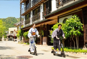 実証実験の特例として、ヘルメットなしで電動キックボードに乗って城崎温泉街を巡る人たち＝豊岡市内（豊岡市提供）