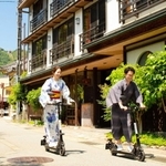 実証実験の特例として、ヘルメットなしで電動キックボードに乗って城崎温泉街を巡る人たち＝豊岡市内（豊岡市提供）