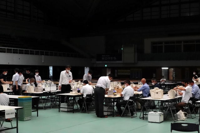 照明が半分落ち、薄暗くなった開票所で票を再集計する職員ら。空調も切れ、扇子であおぐ姿も見られた＝西宮市立中央体育館