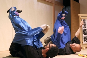 笑福亭鶴笑さん（右）の指導の下、パペット落語に挑戦する筆者。青色の妖怪を表現したいのだが、脚がうまく伸ばせず苦戦している＝神戸市兵庫区、神戸新開地・喜楽館（撮影・長嶺麻子）