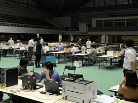 照明が半分落ち、薄暗くなった開票所で票を再集計する職員ら。空調も切れ、扇子であおぐ姿も見られた＝１９日午前１時３６分、西宮市立中央体育館