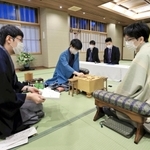 立会人の広瀬章人八段（左）から封じ手を示される豊島将之竜王（手前右）。左から２人目は着手する藤井聡太王位＝１４日午前、北海道旭川市、花月会館