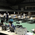 照明が半分落ち、薄暗くなった開票所で票を再集計する職員ら。空調も切れ、扇子であおぐ姿も見られた＝１９日午前１時３６分、西宮市立中央体育館