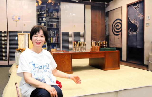仕事場を再現した展示空間を紹介する尼子騒兵衛さん。実際に使った机や画材道具が並ぶ＝尼崎市昭和通２、尼崎市総合文化センター