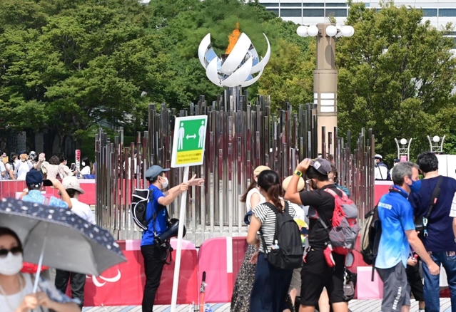 大勢の人が記念撮影を楽しむ「もう一つの聖火台」。係員は「フィジカルディスタンスの確保」を訴えるプラカードを掲げる＝東京都江東区有明３