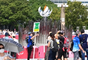大勢の人が記念撮影を楽しむ「もう一つの聖火台」。係員は「フィジカルディスタンスの確保」を訴えるプラカードを掲げる＝東京都江東区有明３