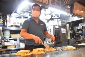 手際よくお好み焼きを焼く店長の沖中幸夫さん。持ち帰りの注文も次々と入る＝広島市中区新天地