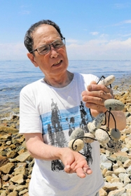 不発弾で指を負傷した中田誠さん。故郷の海に立ち、平和の尊さをかみしめる＝淡路市野島轟木