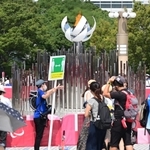 大勢の人が記念撮影を楽しむ「もう一つの聖火台」。係員は「フィジカルディスタンスの確保」を訴えるプラカードを掲げる＝東京都江東区有明３