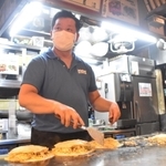 手際よくお好み焼きを焼く店長の沖中幸夫さん。持ち帰りの注文も次々と入る＝広島市中区新天地