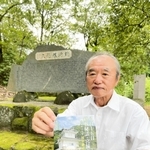 龍野公園の顕彰碑を背に、田中静壱の評伝小説を持つ筆者の横家伸一さん＝たつの市龍野町下霞城