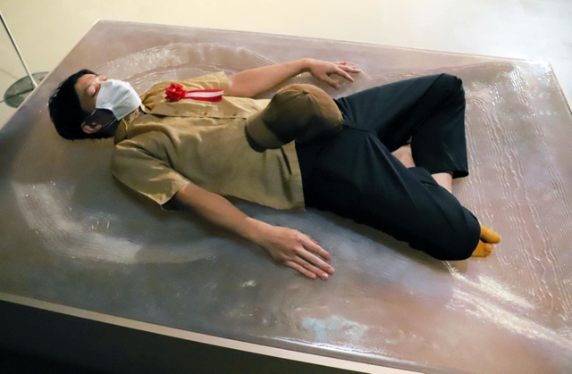 「とろける身体－古墳をひっくり返す」に寝転ぶ作者の岡本高幸さん＝大阪府吹田市千里万博公園、国立民族学博物館